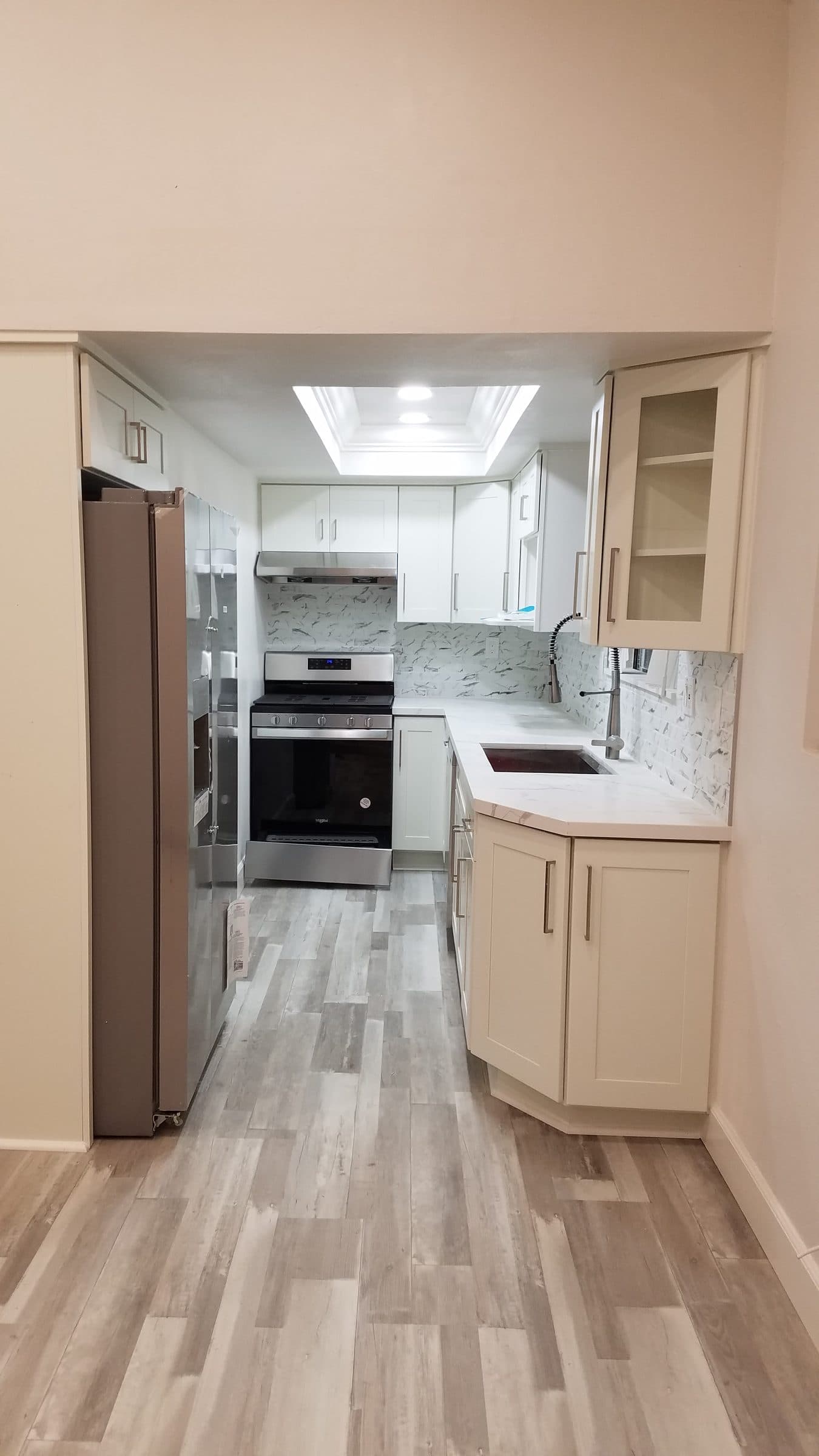 Galley kitchen with white shaker cabinets, stone-look backsplash, stainless appliances and wood-look plank flooring