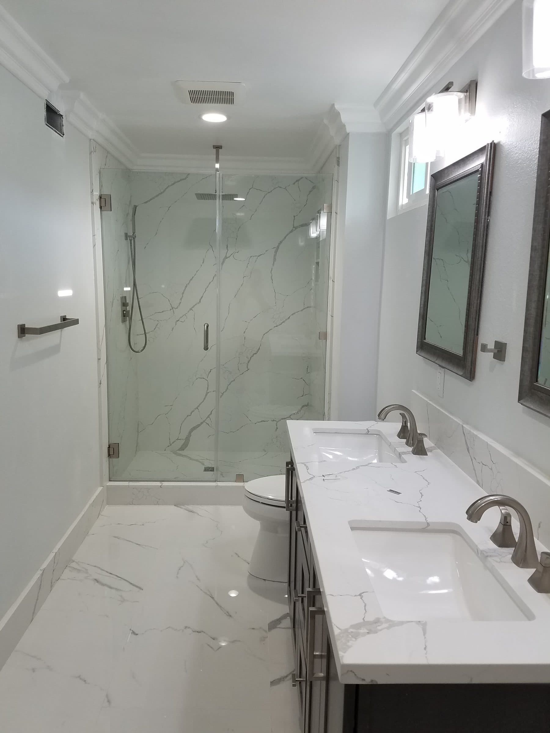 Remodeled bathroom with a frameless glass walk-in shower, marble-look tile and a double vanity