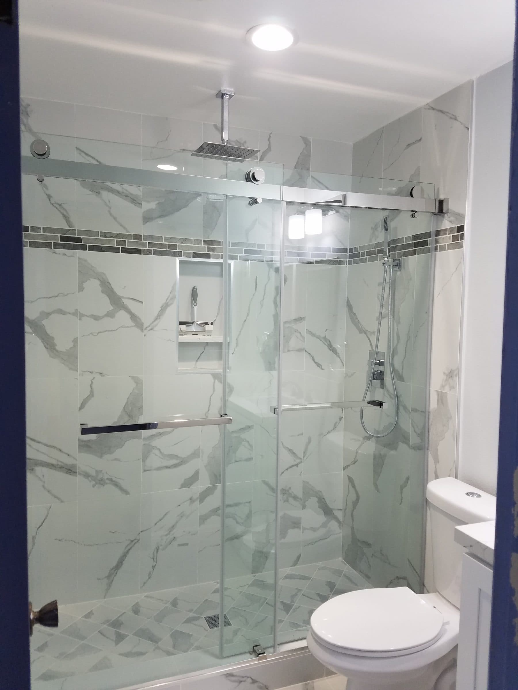 Shower with a sliding glass door, marble-look wall tile, mosaic accent band and recessed niche
