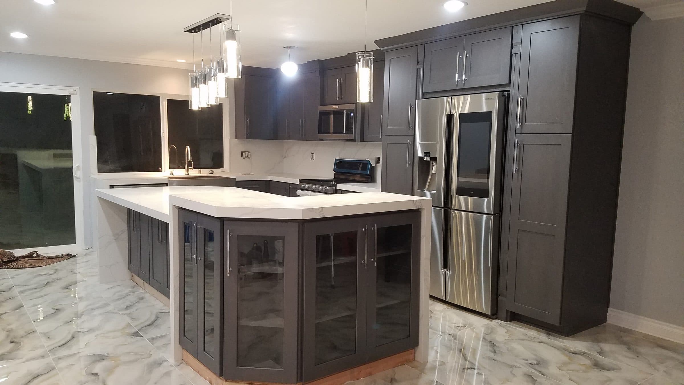 Remodeled kitchen with charcoal shaker cabinets, a large island with glass-front cabinets, white countertops and pendant lights
