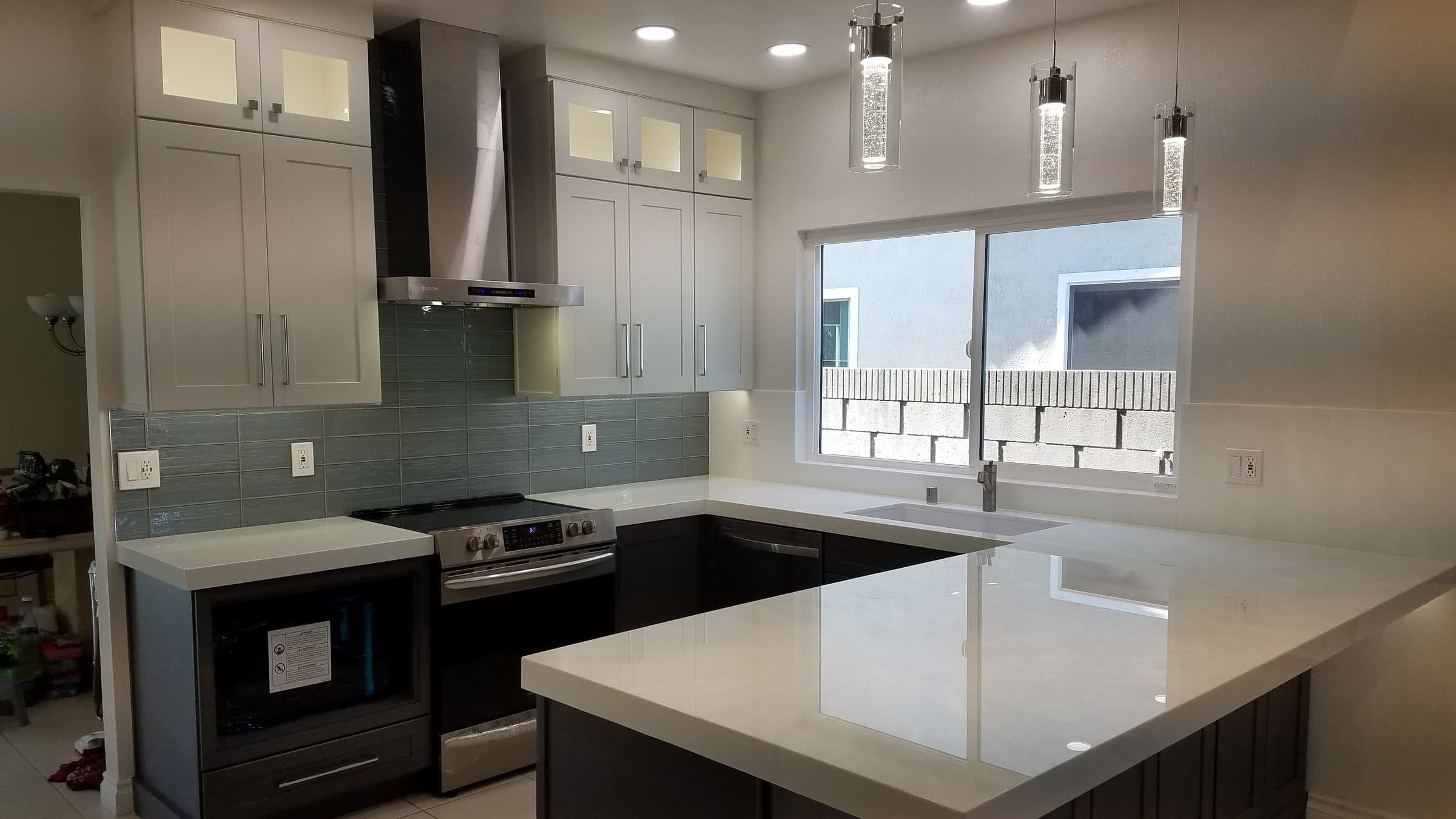 Remodeled kitchen with white glass-front upper cabinets, gray lower cabinets, blue-gray glass tile backsplash and white countertops