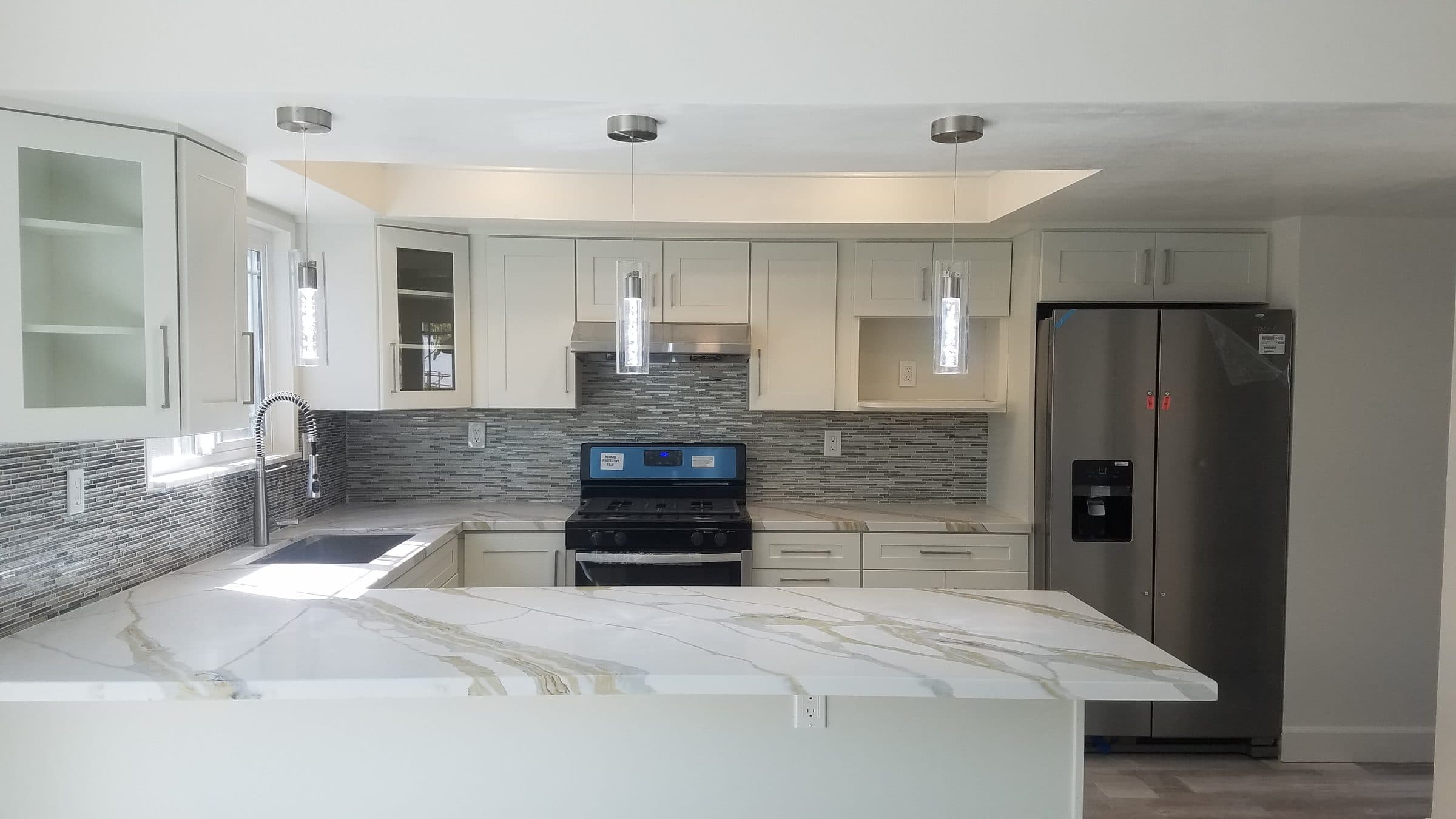White shaker kitchen with mosaic tile backsplash, marble-look countertops with gold veining and pendant lights